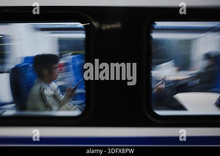 A train rushes by, yet passengers inside sit still, absorbed in their phones. Motion and stillness contrast—two worlds in one frame, one racing past Stock Photo