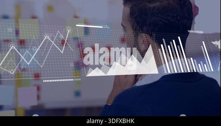 Studying man in sweater-over-shirt analyzing digital line area bar charts at whiteboard, copy space Stock Photo