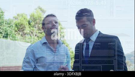 Discussing two businessmen in suit and tie comparing tablet and papers on terrace with HUD charts Stock Photo