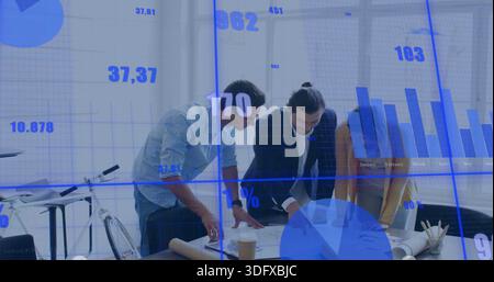 Reviewing three colleagues at meeting table by windows, in mustard, dark blazers, pointing at plans Stock Photo