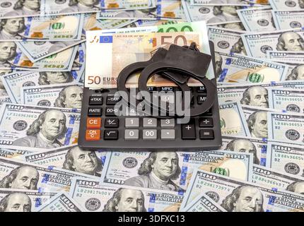 Steel police handcuffs, euro banknotes and calculator lying on the background of american dollars Stock Photo