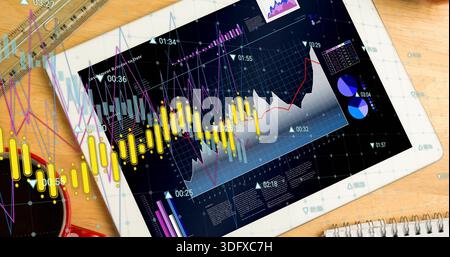 Displaying tablet showing dashboard with yellow candles and line graphs on desk, with red mug Stock Photo