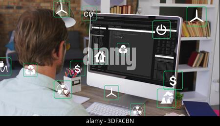 Seated mid-adult man wearing green shirt, glasses, coding on monitor at home, eco icons, copy space Stock Photo
