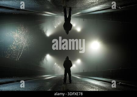 An upside down edit of a spooky mysterious hooded figure. Standing in the road on a foggy winters night Stock Photo