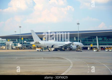A large airplane is parked on the tarmac next to a sleek airport terminal. Ground crews are preparing for loading and maintenance as travelers await d Stock Photo
