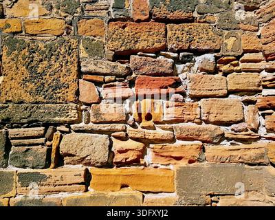 A rustic and unique stone wall featuring natural earth tones such as yellow, copper, orange, and sand, composed of stones in various sizes. Stock Photo