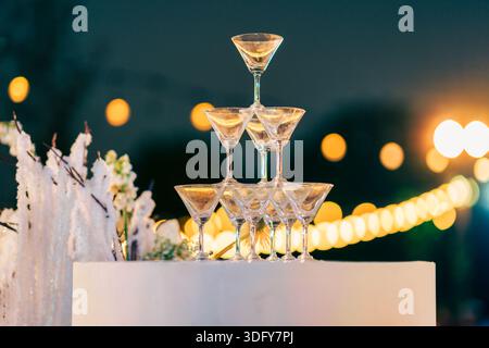 Stacked cocktail glasses with blurred golden bokeh on event table in wedding celebration Stock Photo