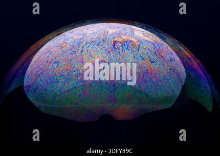 Vivid close-up of a soap bubble surface, showcasing swirling rainbow colors on a dark background, ideal for creative and scientific concepts. Stock Photo