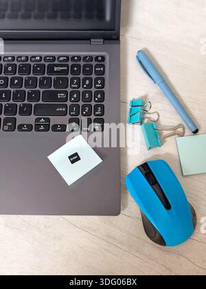 Workplace with laptop, blue wireless mouse, envelopes, notebook, office desk, sticky notes on a light wooden desk. Business, planning, remote work Stock Photo
