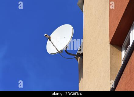 Satellite Dish mounted on brick wall against blue sky background Stock Photo