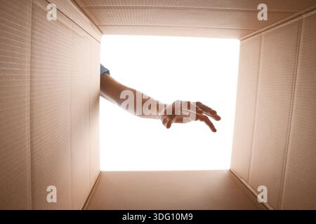 Man reaching into cardboard box against white background, closeup. View from inside package Stock Photo