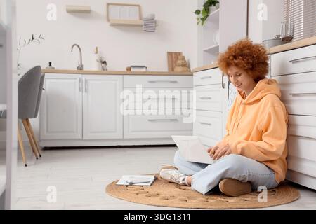 Redhead female freelancer working with laptop in kitchen Stock Photo