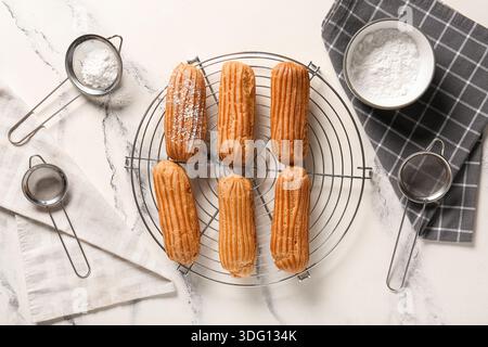 Grid with tasty eclairs, sieves and bowl of sugar powder on marble background Stock Photo