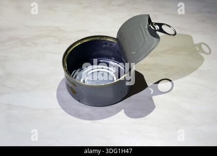 open and empty rounded can on a table with its  shadow on a table surface Stock Photo