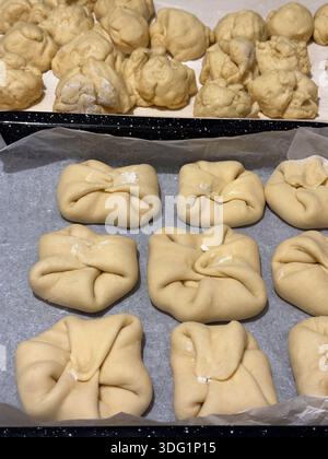 Balls and folded dough arranged on trays, ready for baking. Some dough portions are scrunched while others neatly folded, all resting on parchment pap Stock Photo