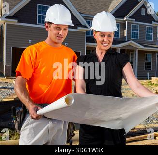 At a sunlit build site, a construction worker and an engineer study blueprints together, measuring lines and discussing details as framing rises, team Stock Photo