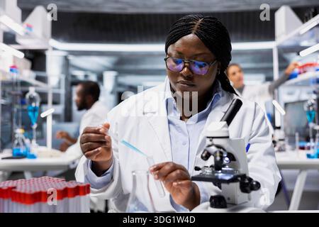 Histology technician in laboratory pipets agent into blue test tube sample to improve chemical formulation efficiency. Lab staff member observes reaction in test tube to verify scientific hypothesis Stock Photo