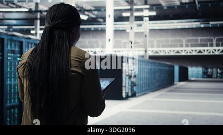 Developer doing data center automation using AI neural networks on tablet. Server room IT professional implements deep learning driven predictive maintenance systems using device, camera A Stock Photo
