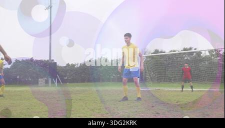 Holding position central player in yellow jersey and blue shorts on grassy pitch, goal net Stock Photo