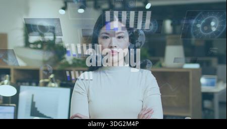 Standing Chinese woman in light knit top crossing arms in modern office, with data overlays Stock Photo