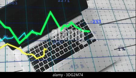 Displaying silver laptop keyboard and trackpad on gridded papers at desk, showing blue grid charts Stock Photo