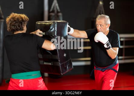 Senior man in boxing gloves punching shield during training Stock Photo
