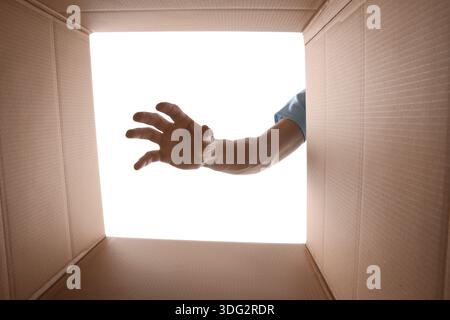 Man reaching into cardboard box against white background, closeup. View from inside package Stock Photo