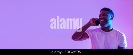 Young Man Enjoys Conversation on Smartphone in Vibrant Neon Light Setting Stock Photo