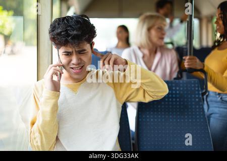 Young asian guy talking on phone plugging ear with finger Stock Photo