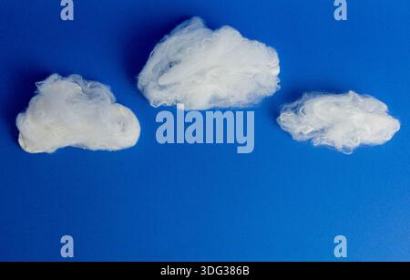 Creative and minimalist composition of white clouds made of textile fiber on a solid blue background, ideal for freedom concepts. Stock Photo