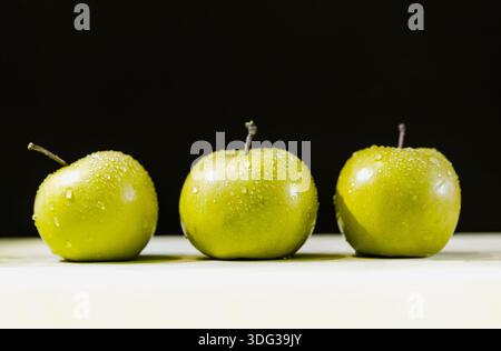 Three apples in a row with drops of water on black and white background Stock Photo