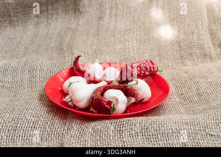 White garlic with red peppers on a red plate. Flat lay with textile background Stock Photo