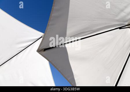 White fabric canopies stretched on metal supports against a clear blue sky, forming abstract geometric shapes. Stock Photo