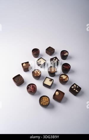 artisanal assorted chocolate bonbons and truffles arranged on a soft white backdrop, minimalist studio with neutral lighting, creamy fillings, nut and Stock Photo