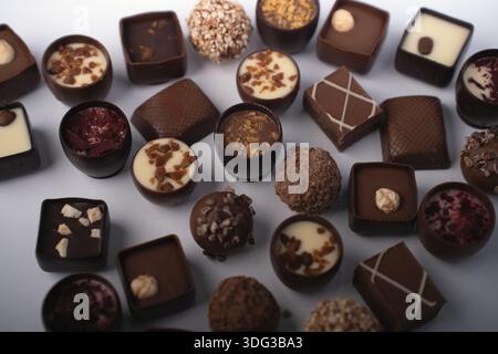 assorted artisanal chocolate bonbons and truffles arranged in a studio flatlay on a pale backdrop, rich dark-and-white chocolate tones, textured toppi Stock Photo