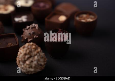 close-up macro of assorted artisanal chocolate truffles and bonbons arranged on a dark tabletop, highlighting textured coatings, cocoa nibs, creamy ga Stock Photo