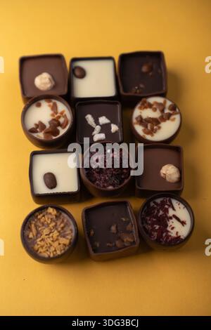 close-up of an assorted grid of artisanal dark and white chocolate pralines and truffles on a warm yellow backdrop, garnished with hazelnuts, caramel Stock Photo