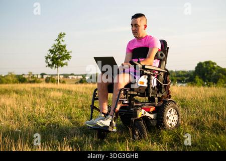 Modern lifestyle and accessibility concept with a wheelchair user working remotely outdoors. Stock Photo