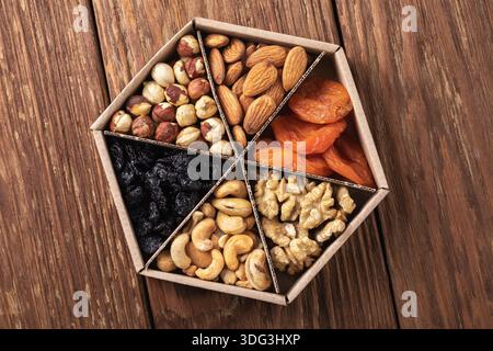 Assorted nuts and dried fruits in a cardboard box on a wooden table, top view, authentic photograph, not AI-generated Stock Photo