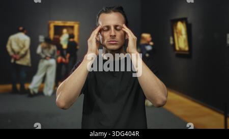 Man young hispanic with raised hand looking at camera among paintings in gallery building; contemplation art appreciation. Stock Photo