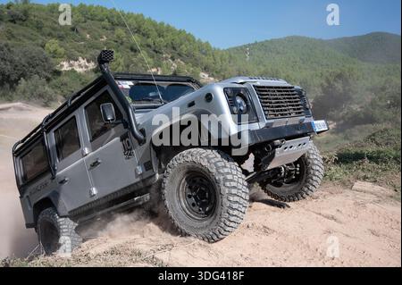 Modified silver Land Rover Defender 110 LWB climbing a steep dirt hill ...