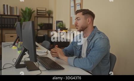 Young man with beard in office engaging in videoconference at desk with computer in professional indoor setting emphasizing modern workplace environme Stock Photo