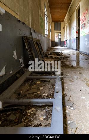 Kastoria, Greece - January 10,2026. Discarded wooden frames lie broken on the floor of a derelict hallway covered in graffiti and decay Stock Photo