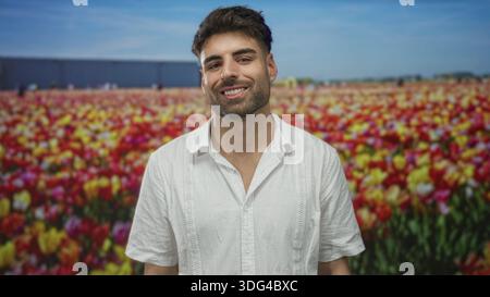 Man wearing a white shirt smiling in a vibrant tulip field studio setting while tilting his head gently; joy optimism. Stock Photo
