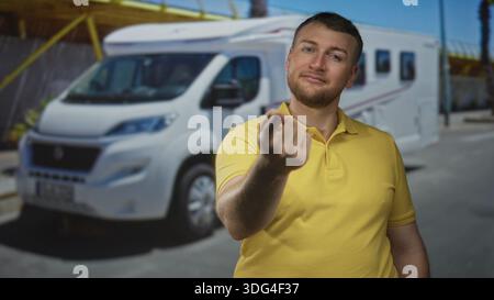 Man in yellow polo beckoning with fingers on street beside white motorhome campervan, smiling and leaning forward toward camera; inviting travel adven Stock Photo