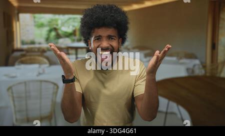 Man expressing emotion indoors in a restaurant setting, showcasing a range of facial expressions with background tables and chairs arranged neatly. Stock Photo