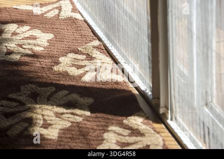 Brown patterned rug next to white sliding glass door frame with screen mesh showing sunny light shadow creates calm peaceful atmosphere in home interi Stock Photo