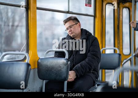 A tired man sleeping in his seat on a tram during his morning or evening commute in an urban setting. employee fell asleep during an early tram ride i Stock Photo
