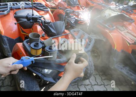Close up hands mechanic holding dirty air filter cleaning dust with air blower gun from orange atv quad bike engine maintenance feeling focused workin Stock Photo