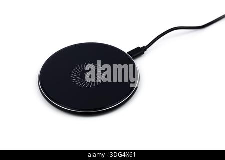 Black round charging pad and connected power cord isolated on white background. Modern technologies concept. Stock Photo